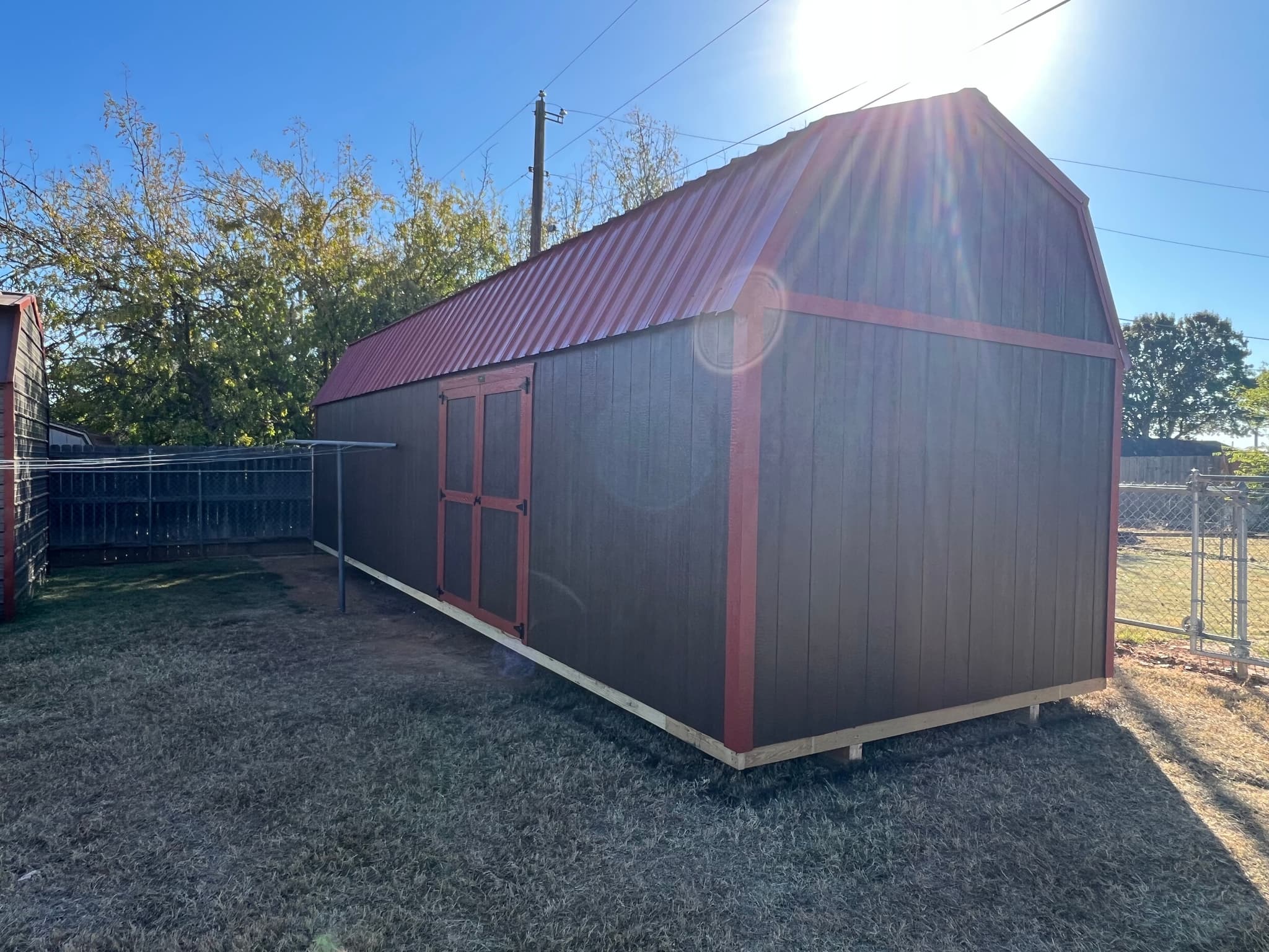 Finished long brown lofted barn garage with red metal roof and red trim in a Wichita Falls backyard.