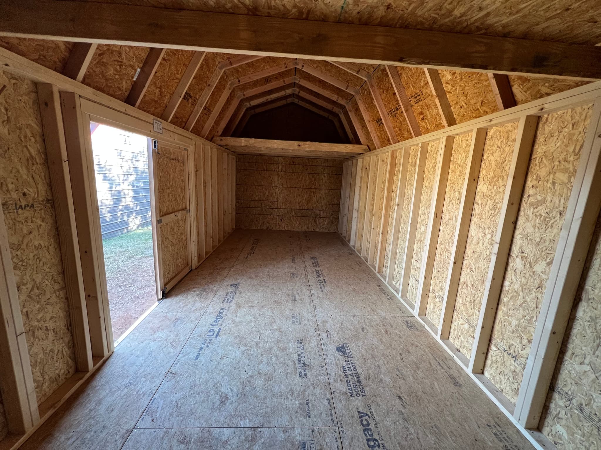 Long interior view of a finished lofted barn garage showing exposed framing, loft, and OSB walls.
