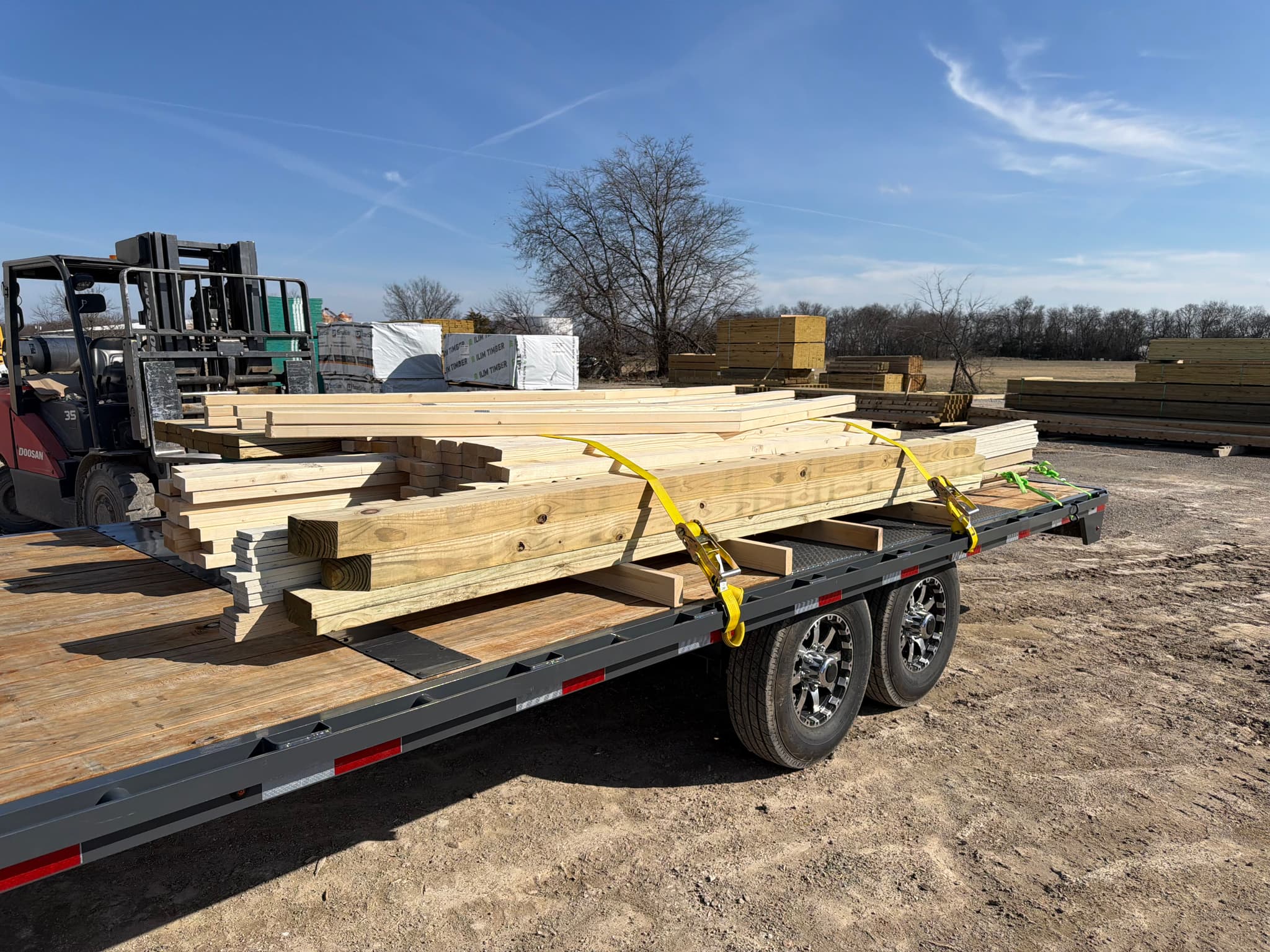 A flatbed trailer at the lumberyard being loaded with framing and panels by a forklift.
